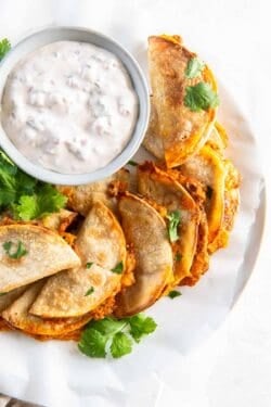 Mini bean and cheese tacos on a white plate with a bowl of creamy salsa dip.