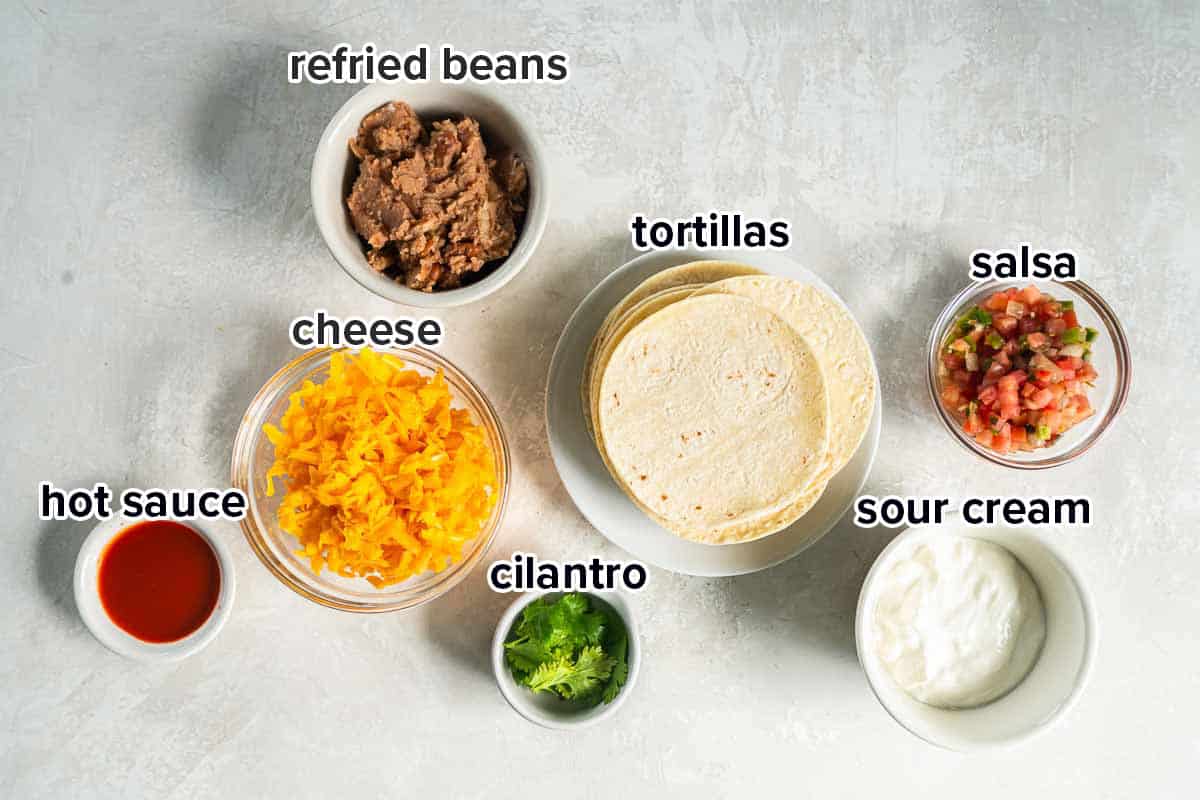 Refried beans, cheese, tortillas and other ingredients in bowls with text.
