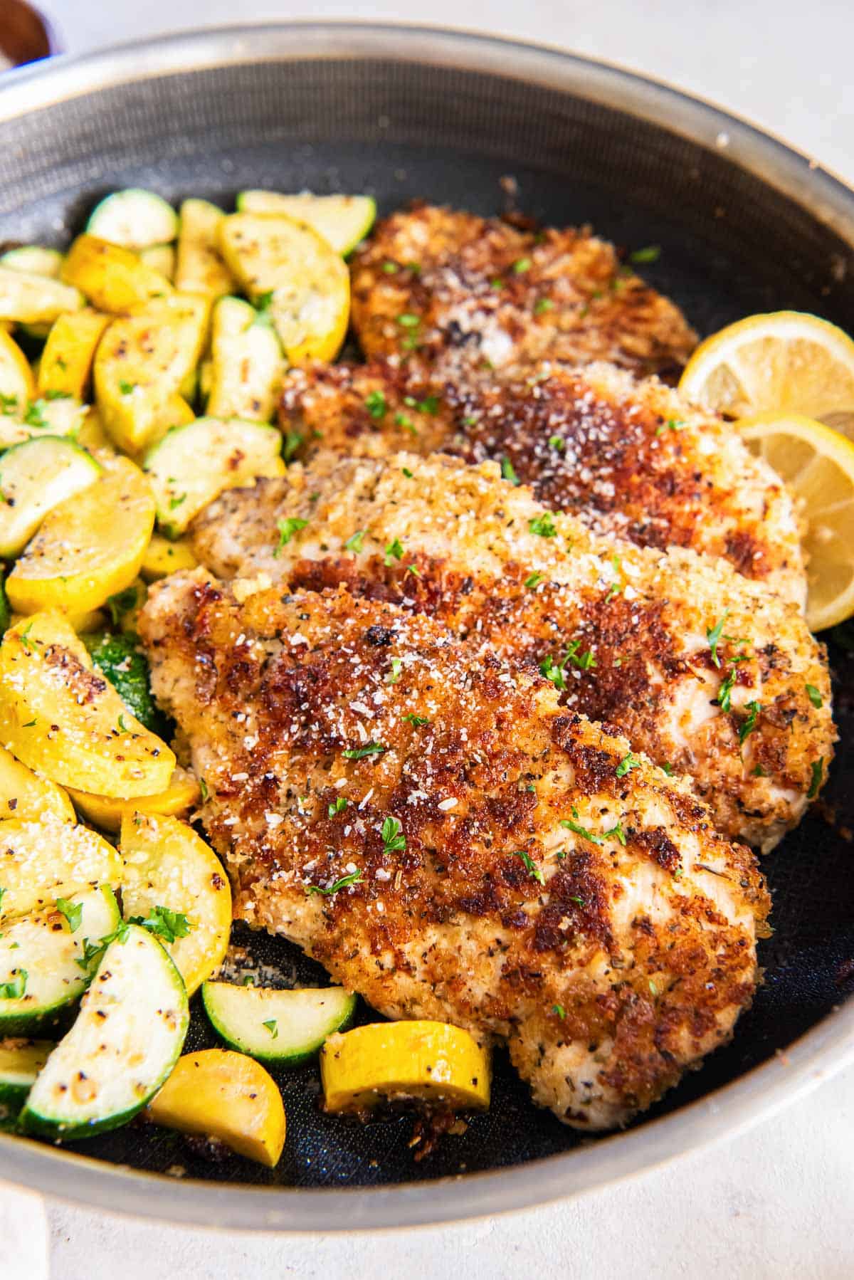 Cooked breaded chicken in a skillet with sliced zucchini.