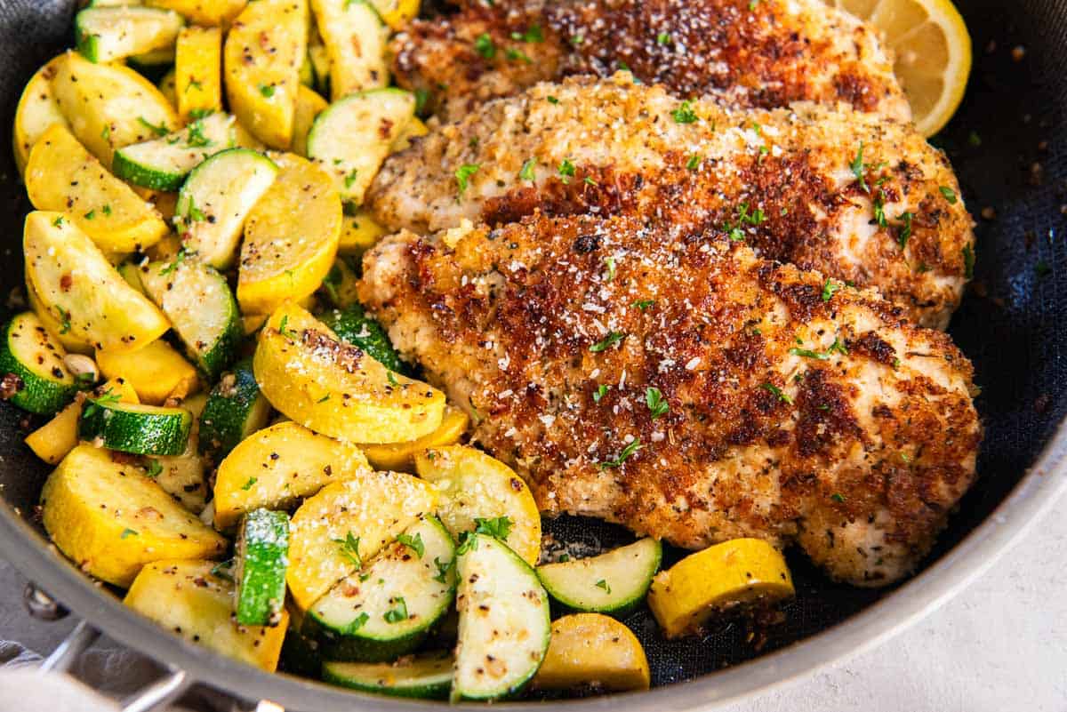 Cooked breaded chicken in a skillet with green and yellow zucchini.
