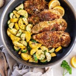 Crispy chicken in a skillet with green and yellow zucchini and lemon slices.