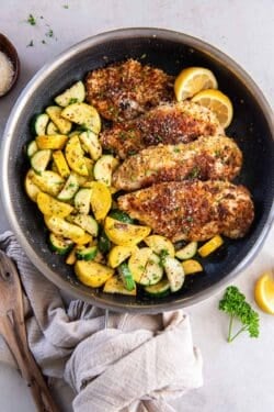 Crispy chicken in a skillet with green and yellow zucchini and lemon slices.