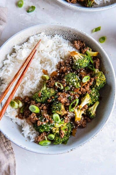 A bowl of white rice and Asian ground beef and broccoli with chopsticks.