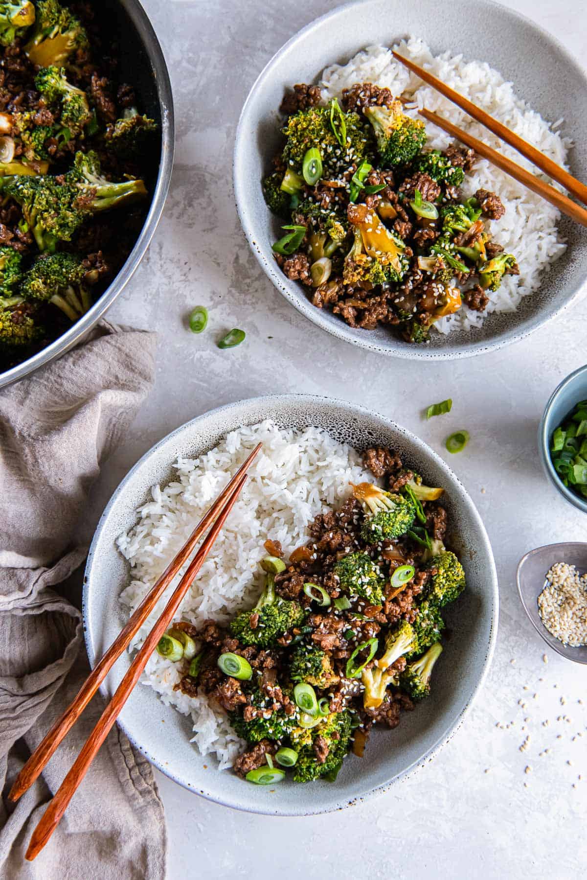 Chopsticks resting on two bowls with white rice and ground beef and broccoli.