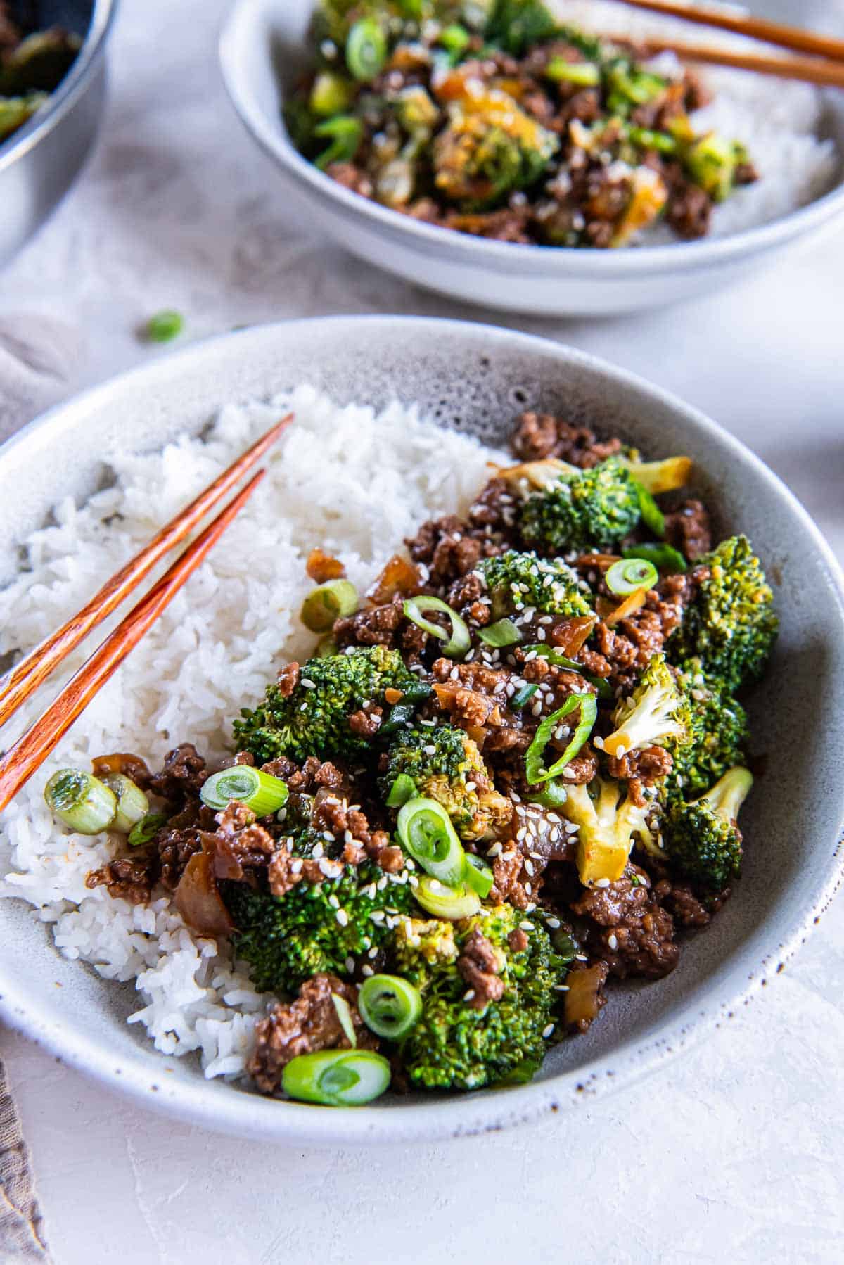 Chopsticks resting in a bowl with Asian ground beef and broccoli and white rice.