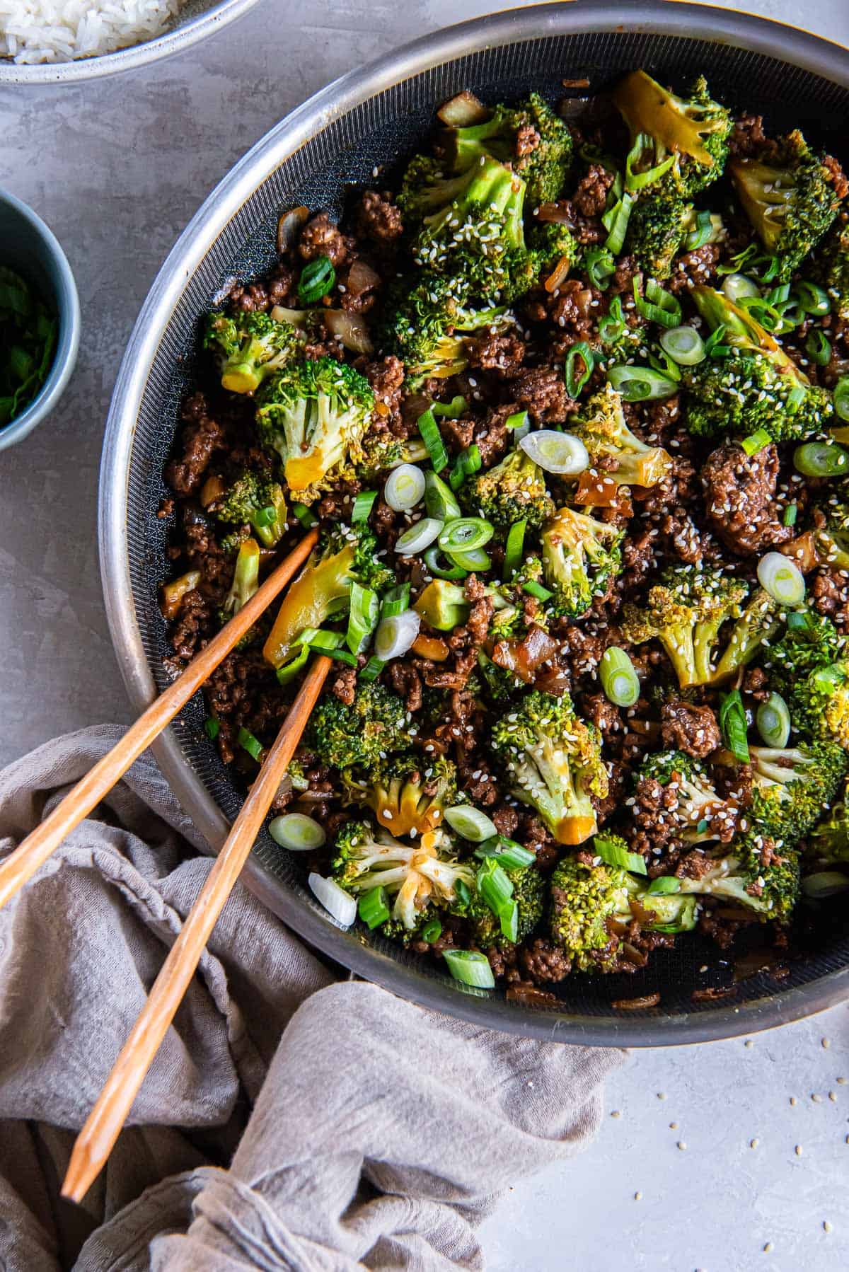 Chopsticks resting in a pan of ground beef and broccoli.