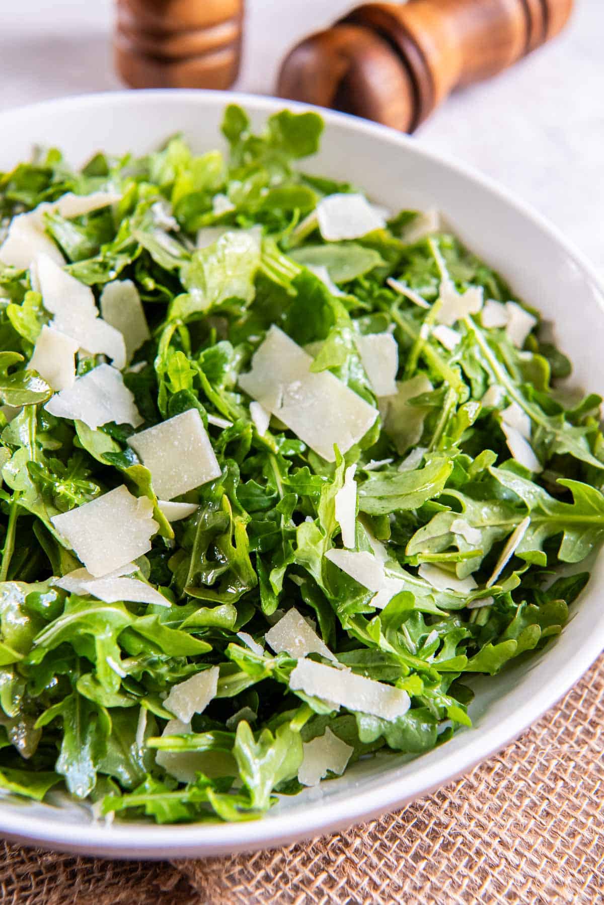 Baby arugula salad topped with shaved Parmesan cheese in a white bowl.