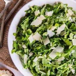 Forks lying next to an arugula salad with shaved Paremsan cheese.