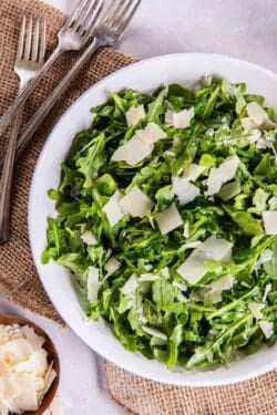 Forks lying next to an arugula salad with shaved Paremsan cheese.