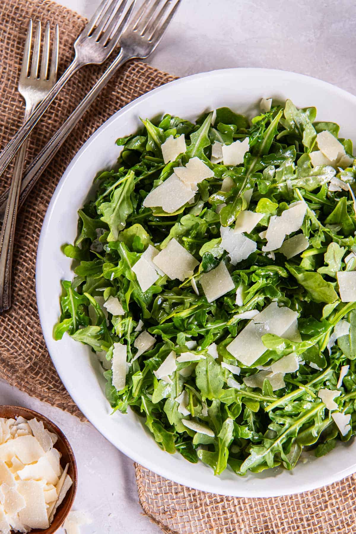 Forks lying next to an arugula salad with shaved Paremsan cheese.