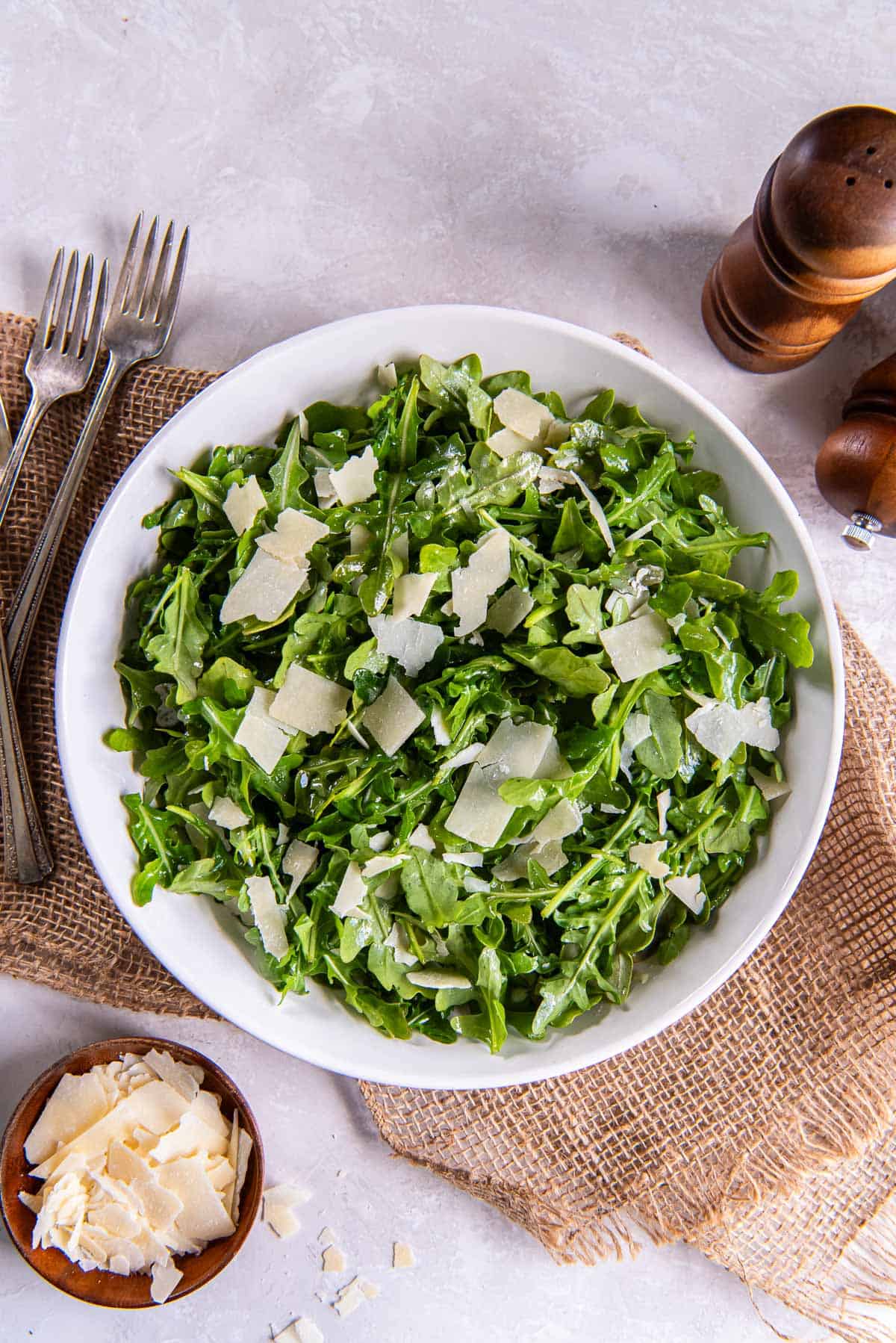 Salt and pepper shakers next to arugula salad in a white bowl.