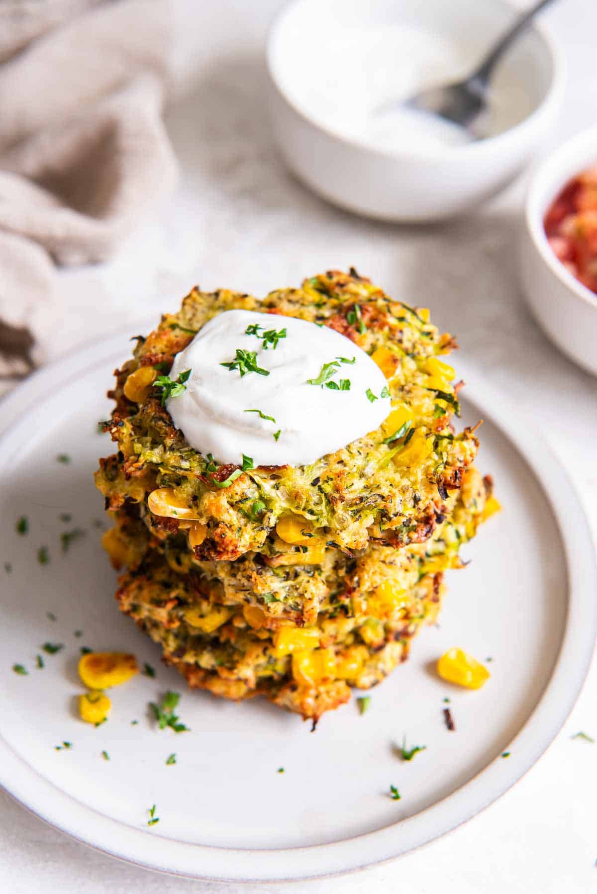 A stack of three zucchini and corn fritters on a plate topped with Greek yogurt.