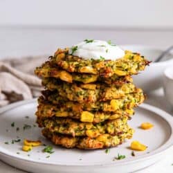 A stack of three zucchini and corn fritters on a plate topped with Greek yogurt.