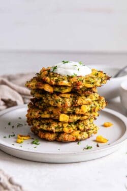A stack of three zucchini and corn fritters on a plate topped with Greek yogurt.