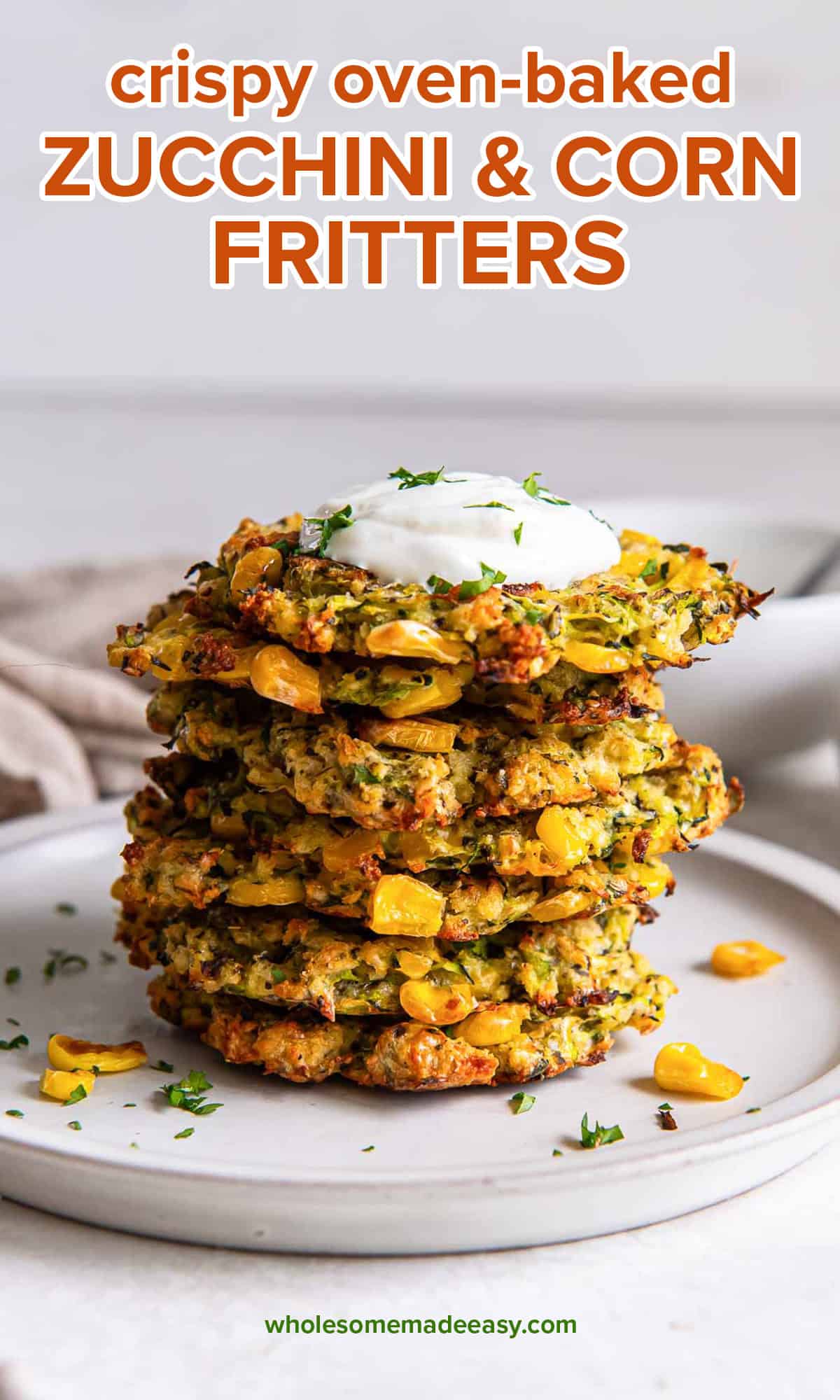 A stack of three zucchini and corn fritters on a plate topped with Greek yogurt with text.