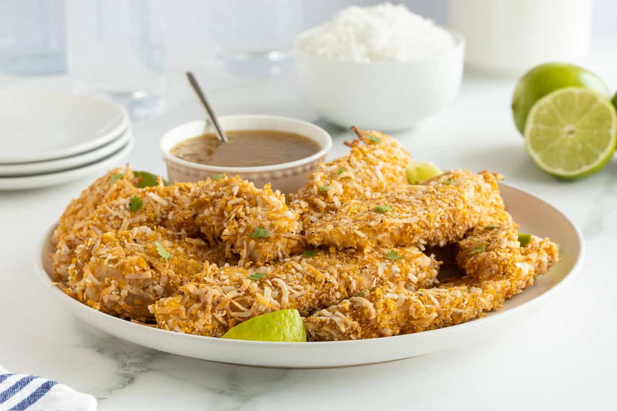 A platter full of coconut chicken tenders with a small bowl of orange dipping sauce.