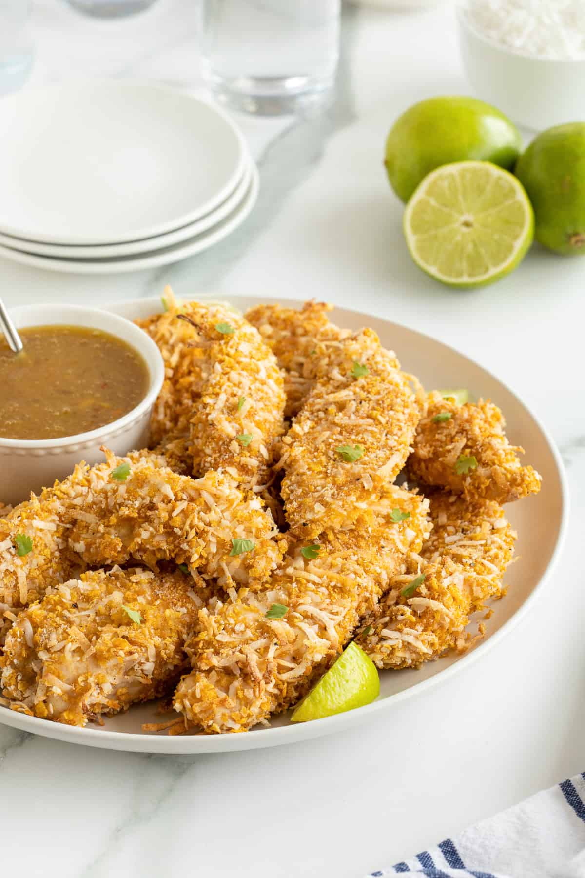 A platter full of coconut chicken tenders with a small bowl of orange dipping sauce.