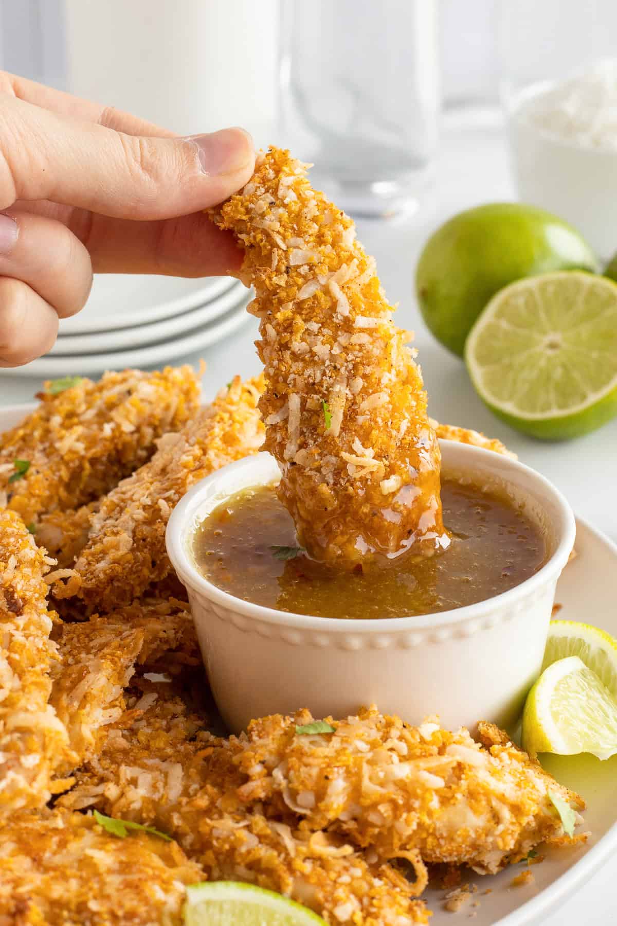 A hand dipping a coconut chicken tender into orange marmalade sauce.