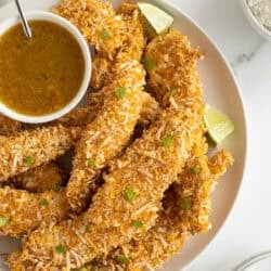 A platter full of coconut chicken tenders with a small bowl of orange dipping sauce.