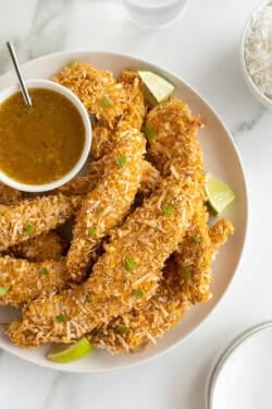 A platter full of coconut chicken tenders with a small bowl of orange dipping sauce.