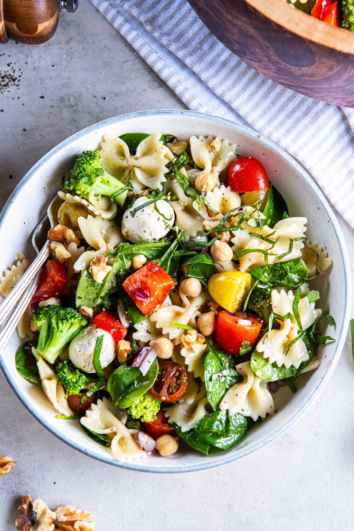 Spinach pasta salad in a small white bowl with forks.