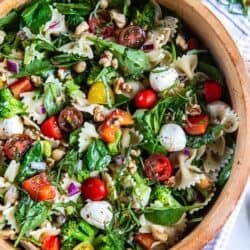 Spinach pasta salad in a wood salad bowl with fresh herbs next to it.
