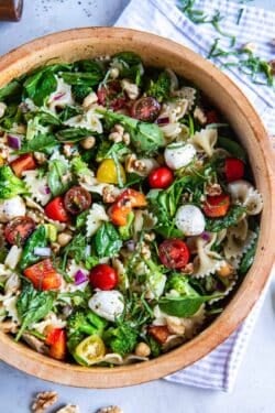 Spinach pasta salad in a wood salad bowl with fresh herbs next to it.