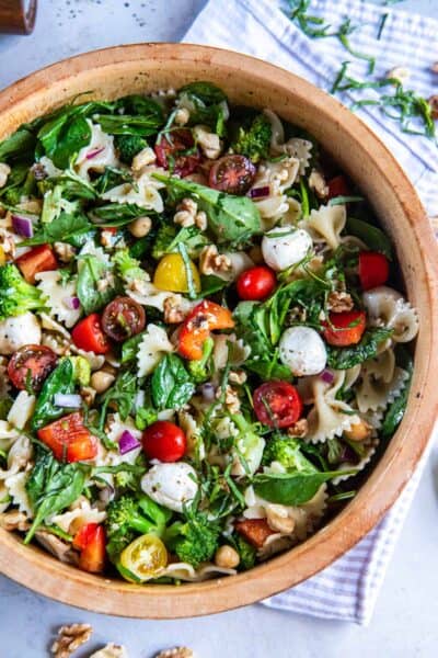Spinach pasta salad in a wood salad bowl with fresh herbs next to it.