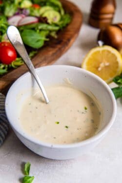Greek yogurt salad dressing in a bowl with a spoon in front of a green salad.