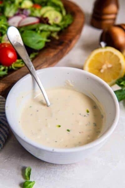 Greek yogurt salad dressing in a bowl with a spoon in front of a green salad.