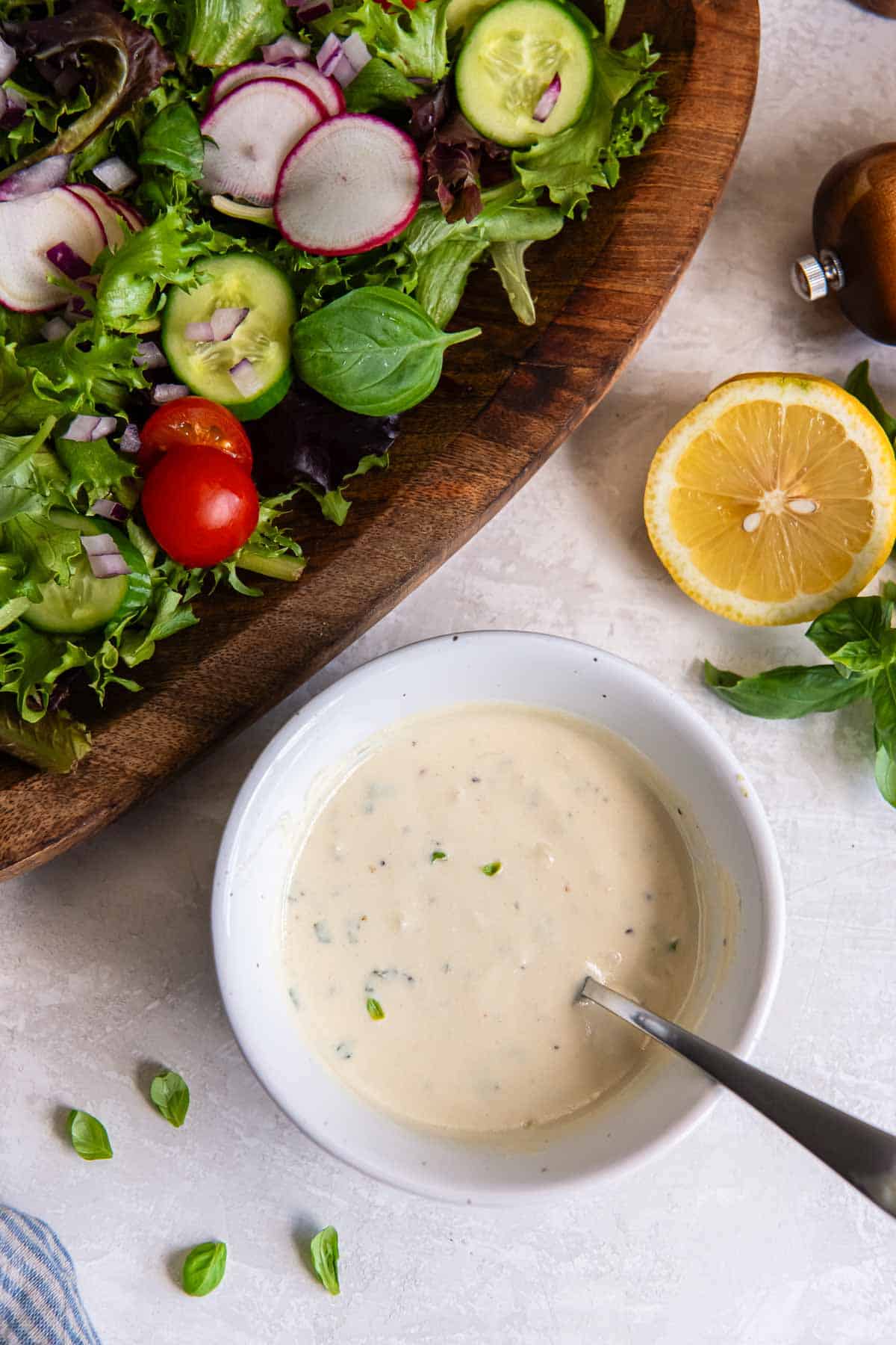 Greek yogurt salad dressing in a bowl with a spoon next to a salad and a lemon half.