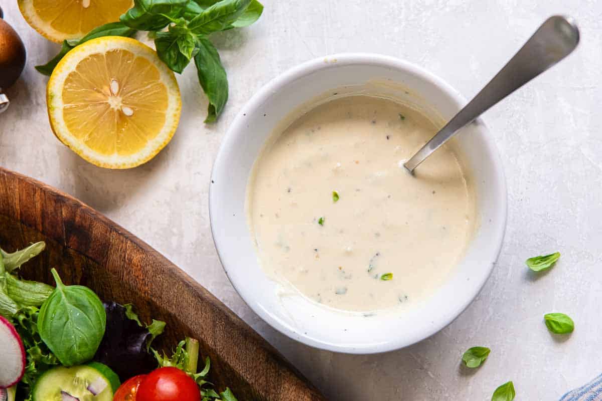 Greek yogurt salad dressing in a bowl with a spoon next to a salad and a lemon half.