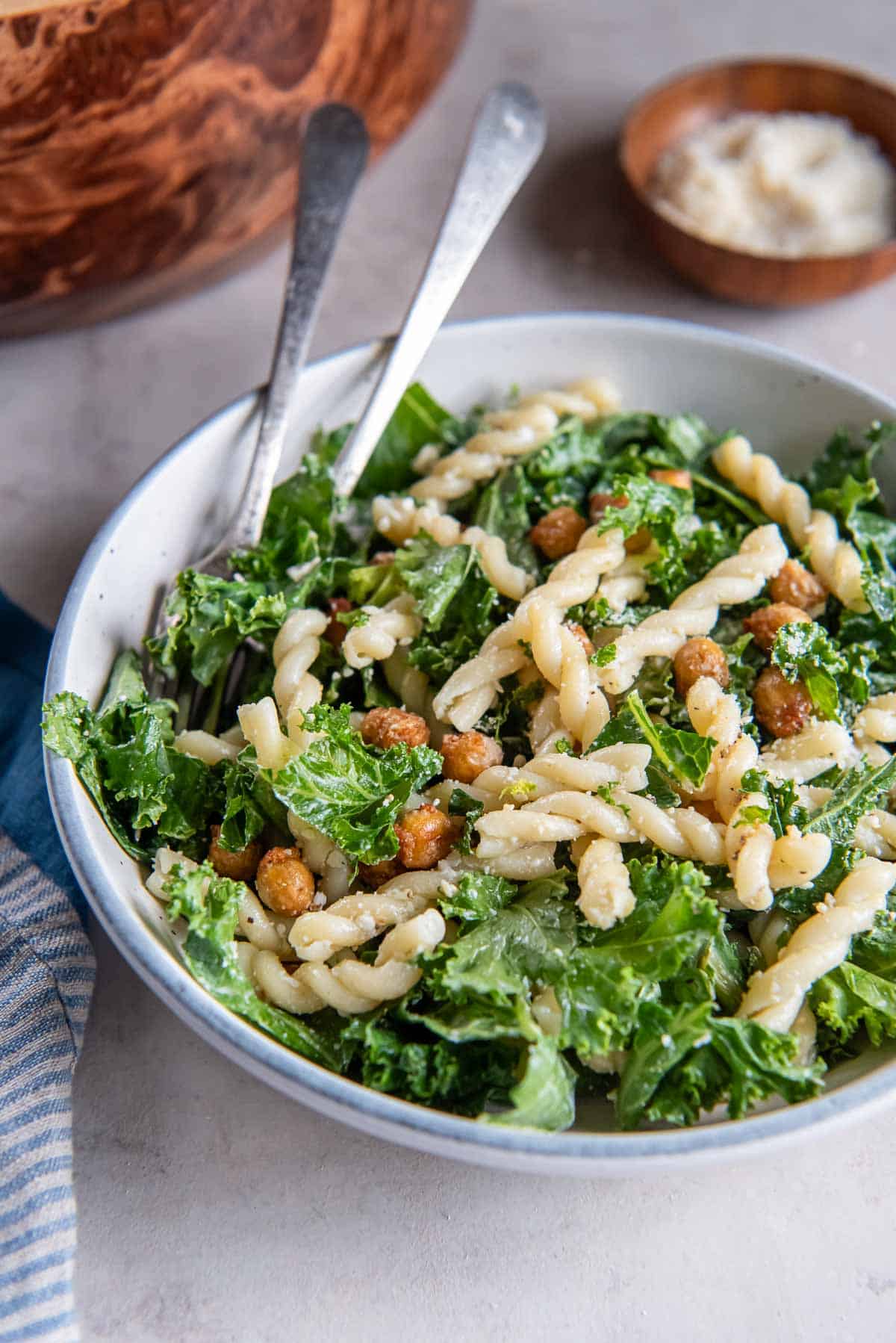 Forks resting in a bowl of kale caesar pasta salad.