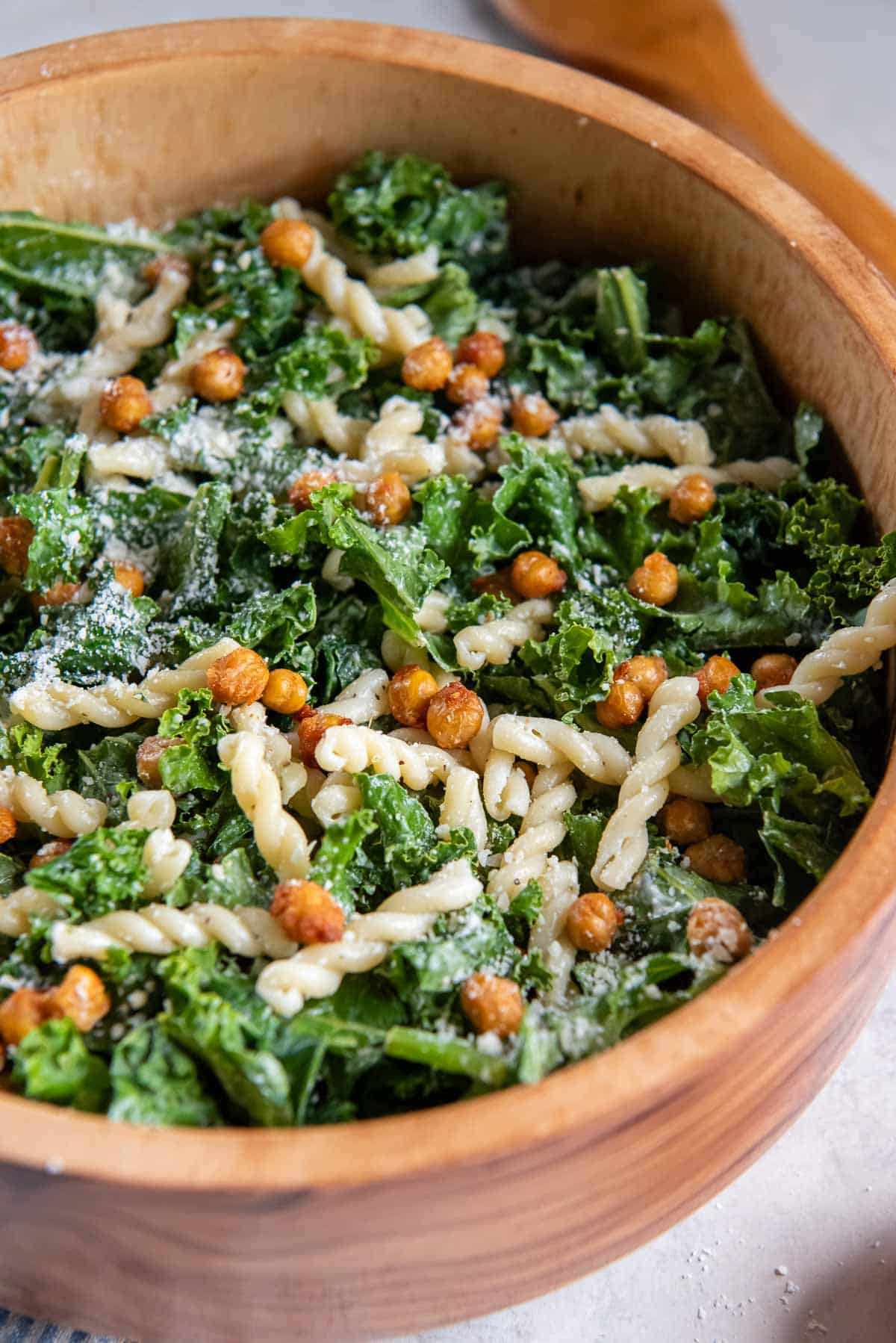 Kale caesar pasta salad with roasted chickpeas in a wood salad bowl.