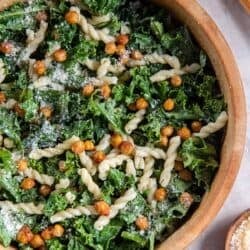 Kale salad with pasta and caesar dressing in a wood salad bowl.