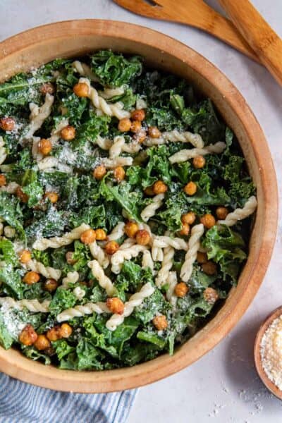 Kale salad with pasta and caesar dressing in a wood salad bowl.