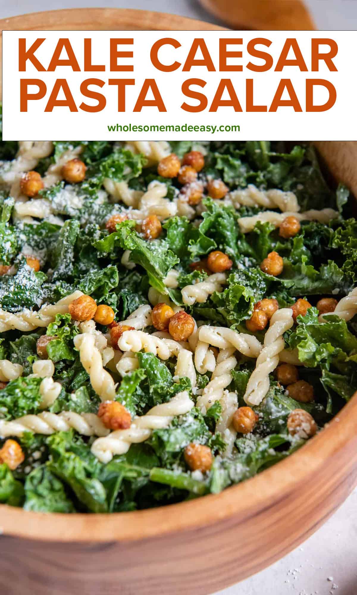 Kale caesar pasta salad with roasted chickpeas in a wood salad bowl with text overlay.