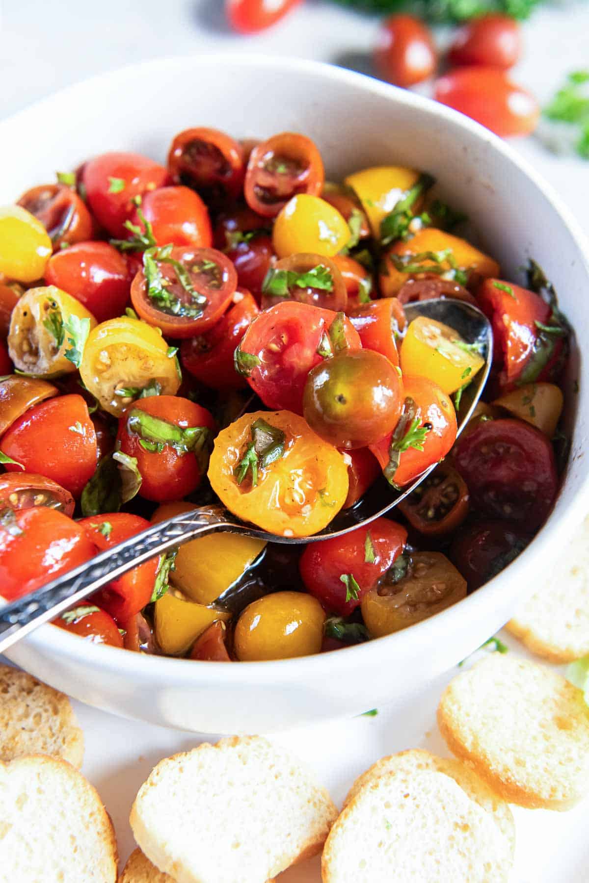 A spoon scooping marinated cherry tomatoes from a white bowl.