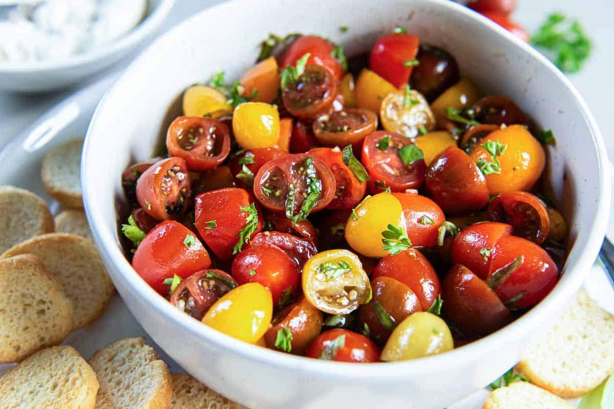 Red and yellow cherry tomatoes in a white bowl with marinade.