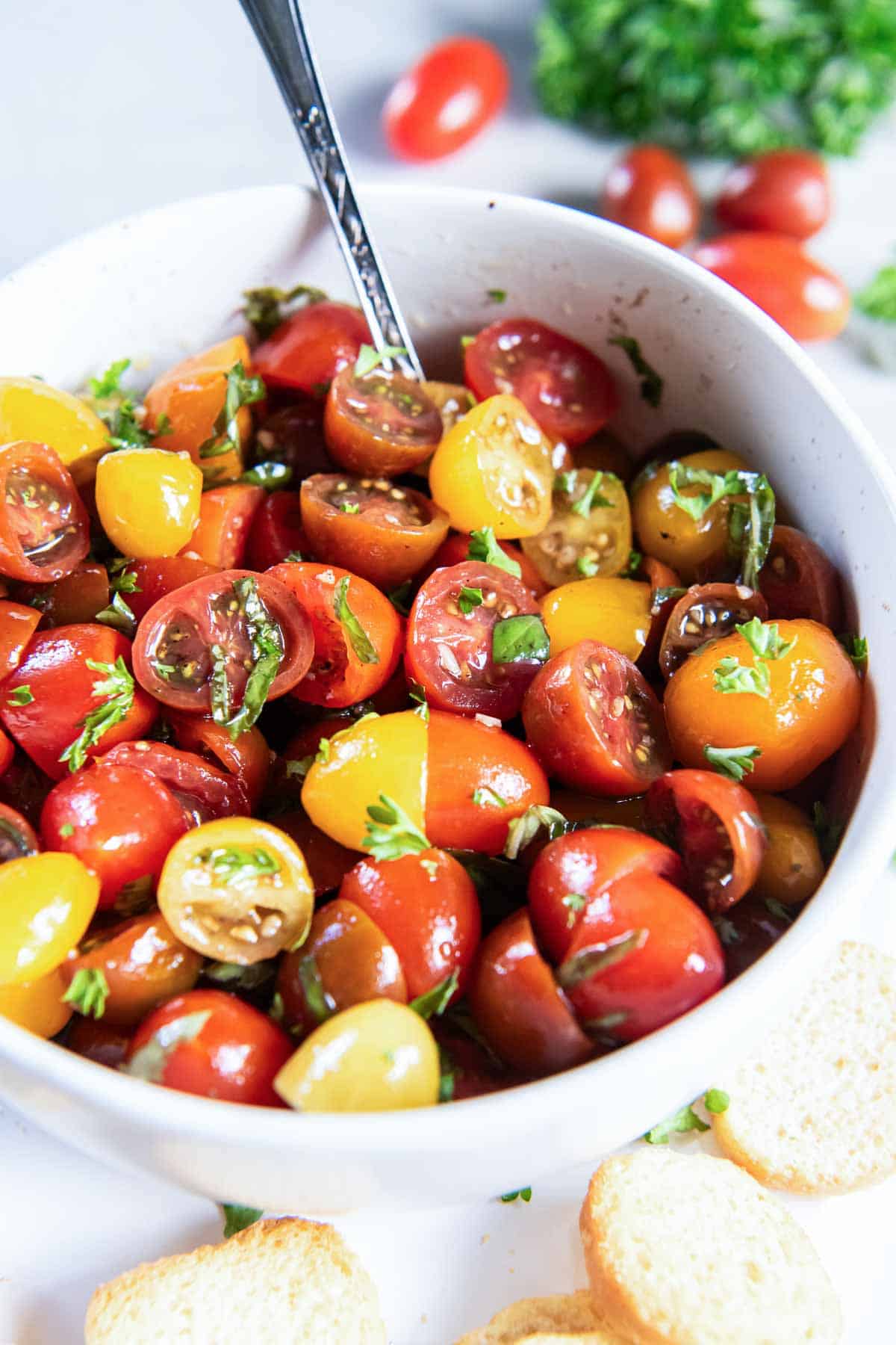 A spoon resting in a bowl of marinated cherry tomatoes.