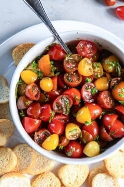 A bowl of marinated cherry tomtaoes surrounded by crostini.
