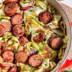 Cabbage and sausage in a pan next to a pepper shaker.