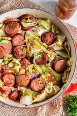 Cabbage and sausage in a pan next to a pepper shaker.