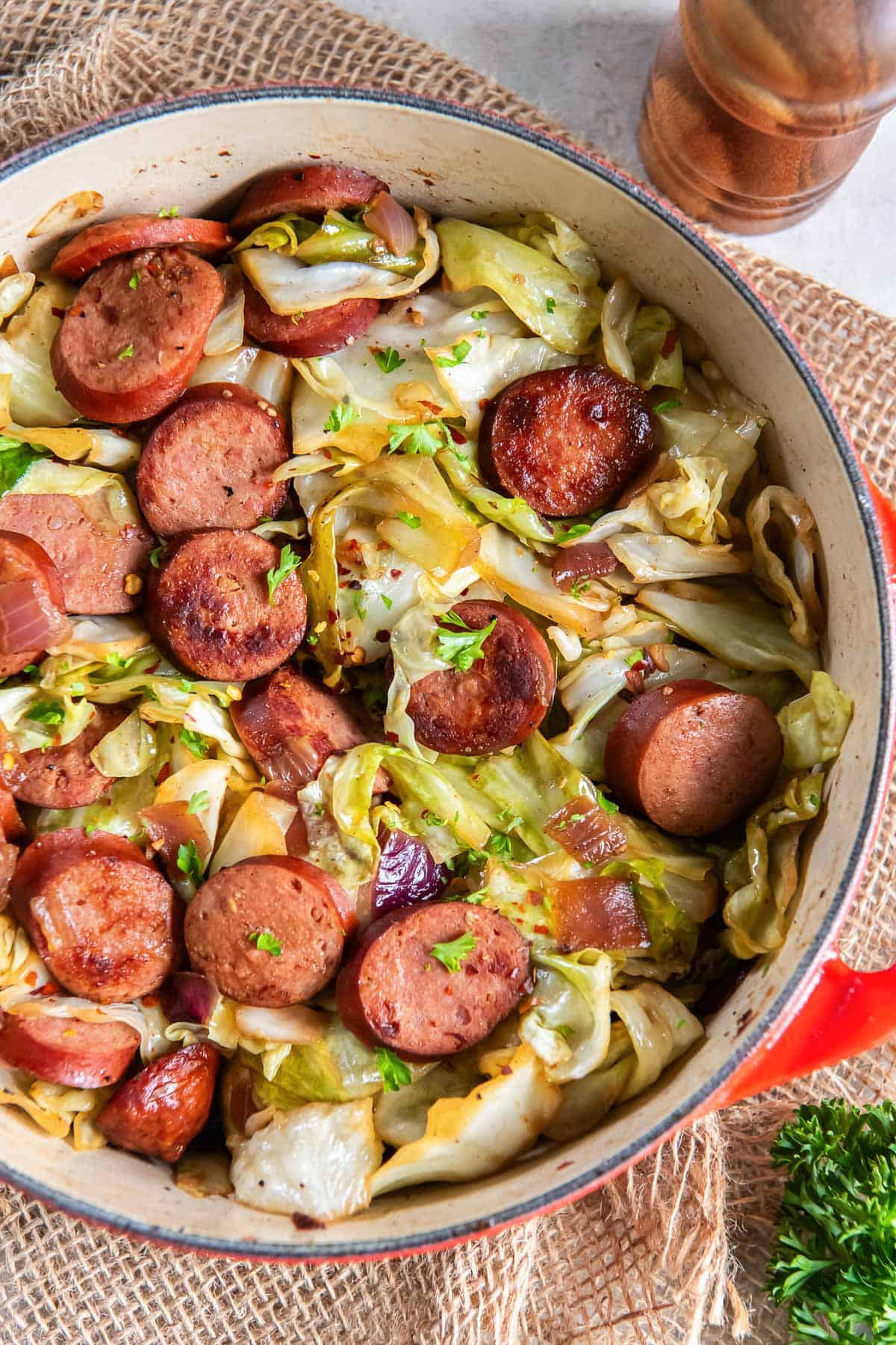 Cabbage and sausage in a pan next to a pepper shaker.