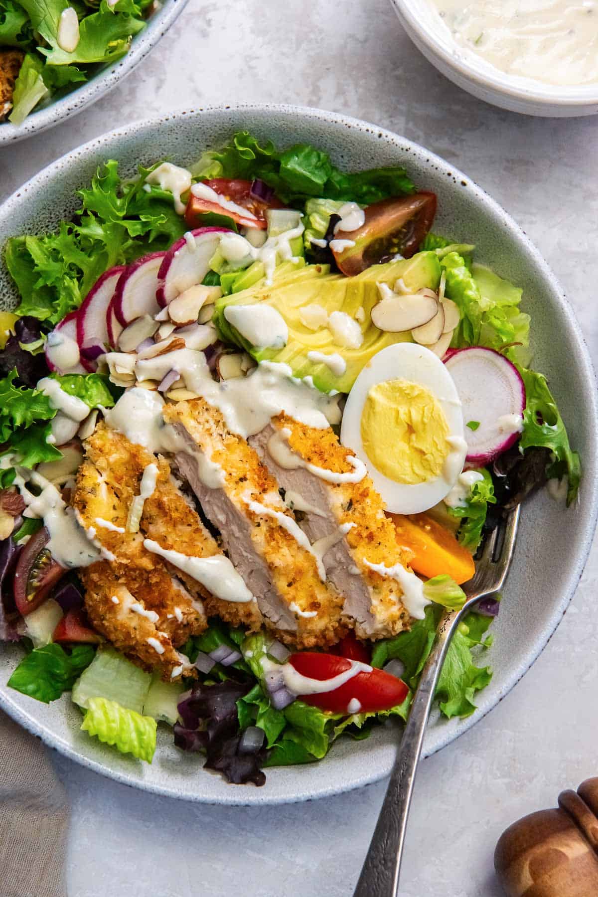 A fork resting in a white bowl filled with crispy chicken salad with greek yogurt dressing.