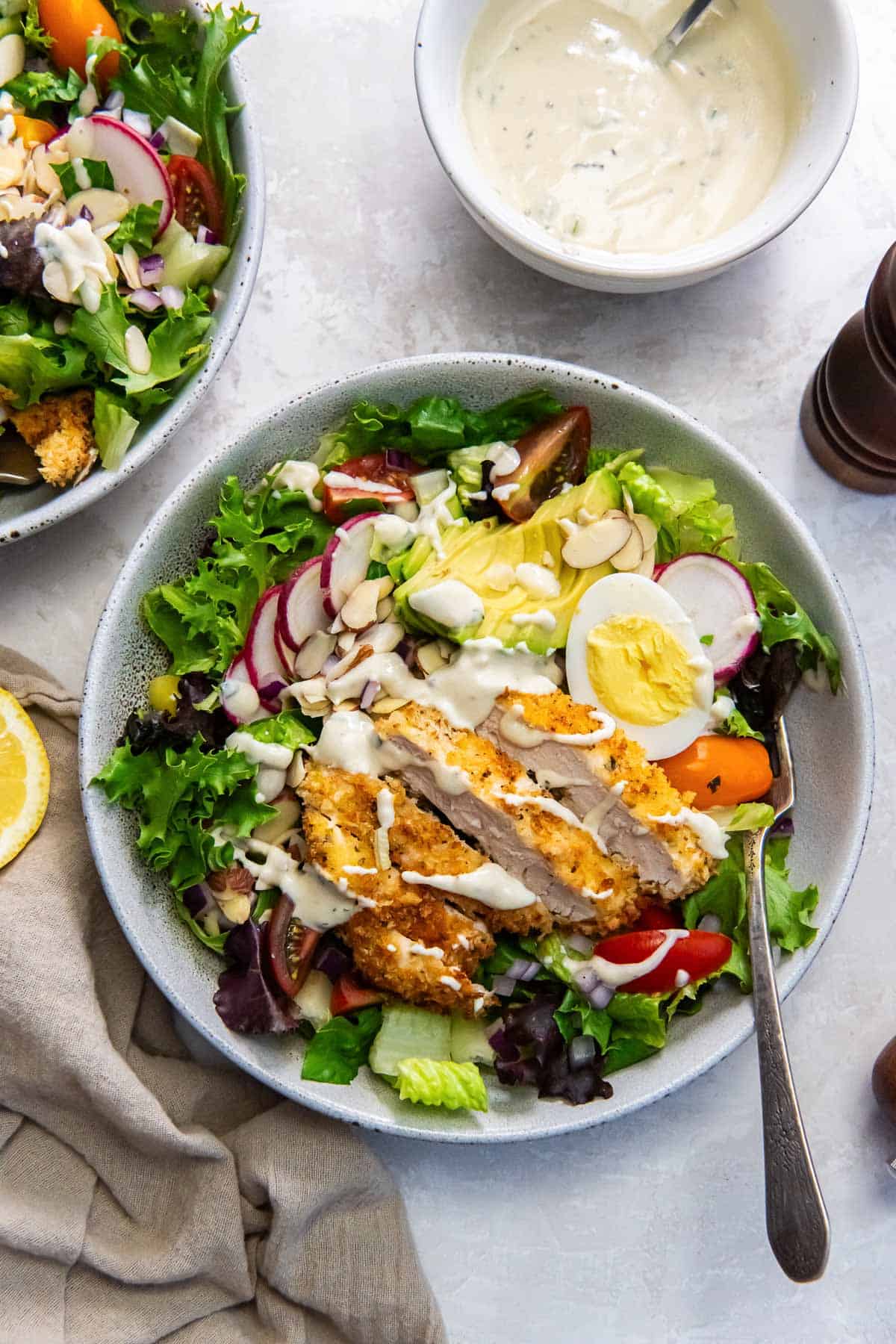 Two bowls of salad with crispy chicken, hard-boiled eggs, radishes and creamy dressing.