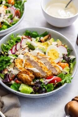 A salad with crispy breaded chicken, avocado, radish, and greek yogurt dressing.