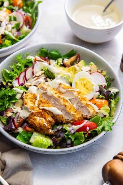 A salad with crispy breaded chicken, avocado, radish, and greek yogurt dressing.
