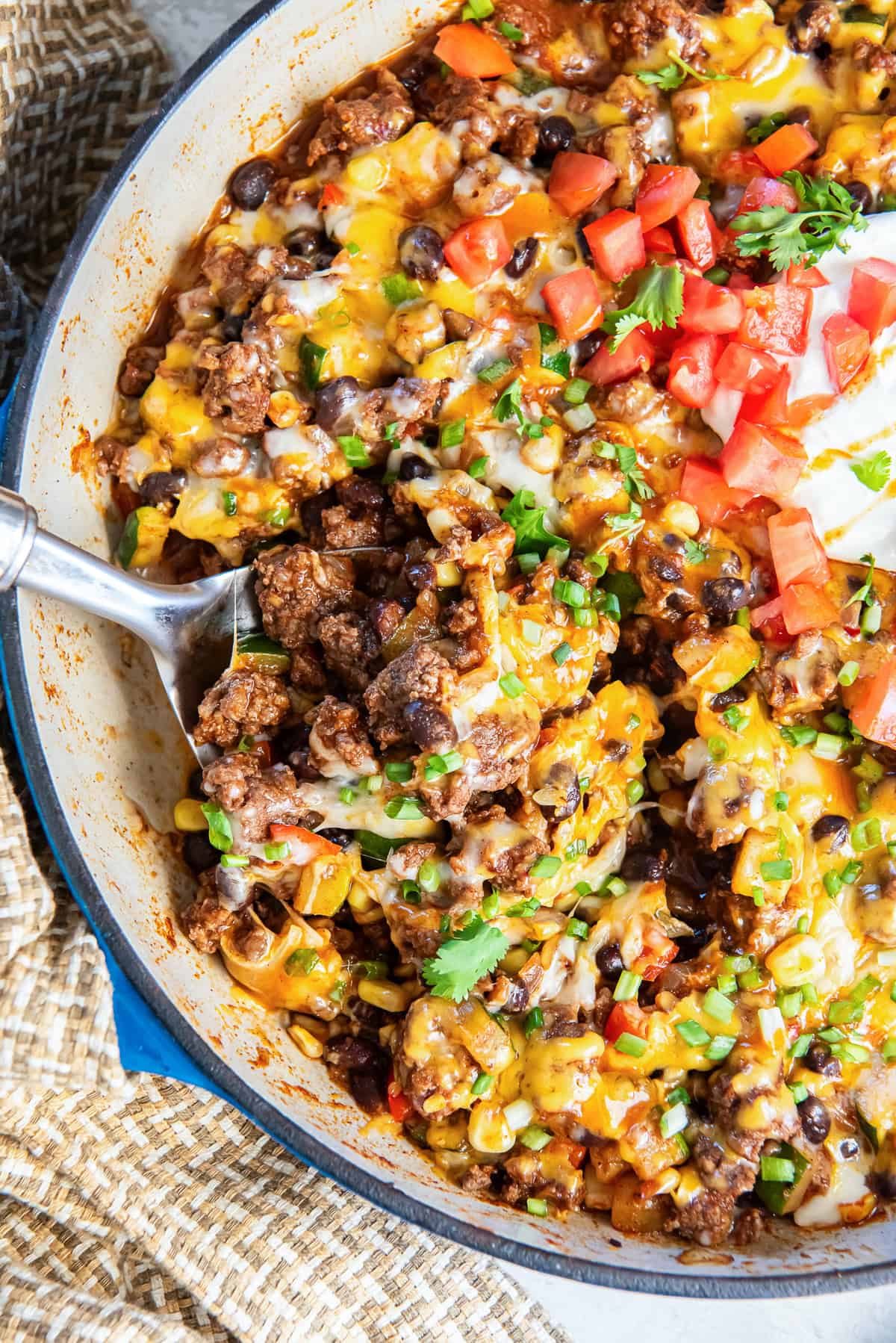 A spoon scooping loaded taco skillet from a pan.