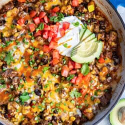 A skillet filled with a beef and bean mixture and topped with sour cream, tomatoes, and sliced avocado.